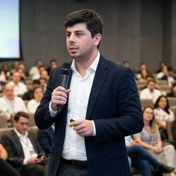Flávio Vieira falando ao microfone em uma palestra, diante da plateia.