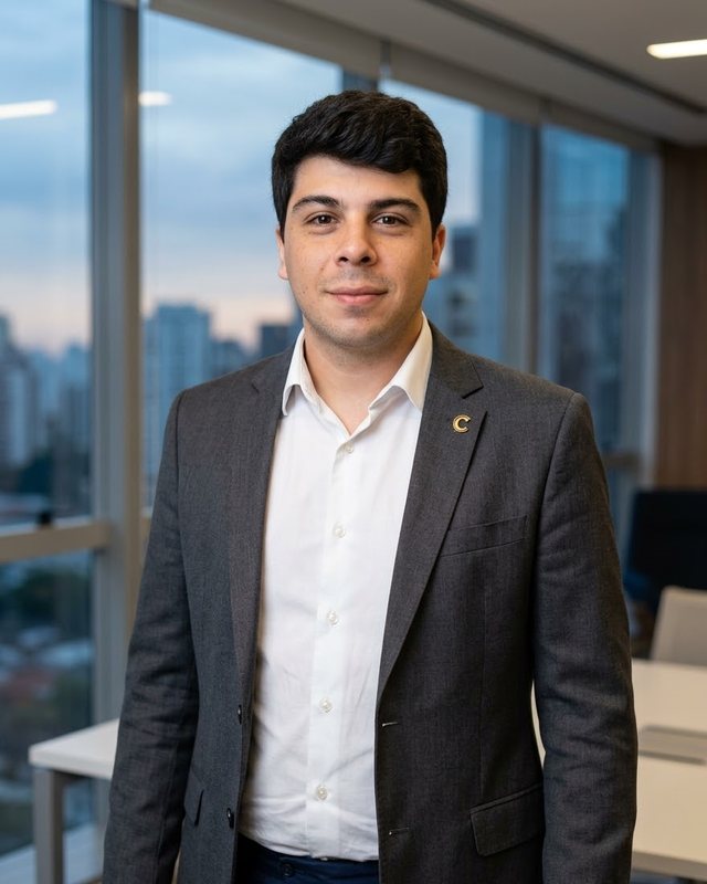 Retrato de Flávio A. Vieira, de terno cinza e camisa branca, sorrindo levemente diante de uma janela com vista da cidade.